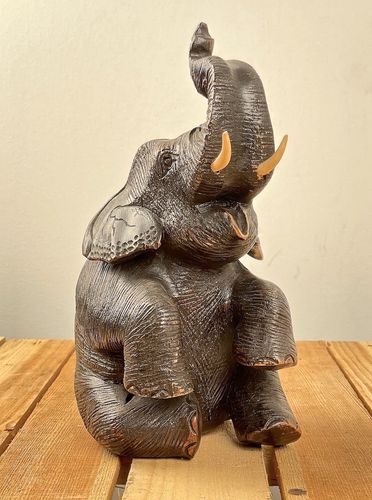 Elefant sitzend mit erhobenem Rüssel aus Holz